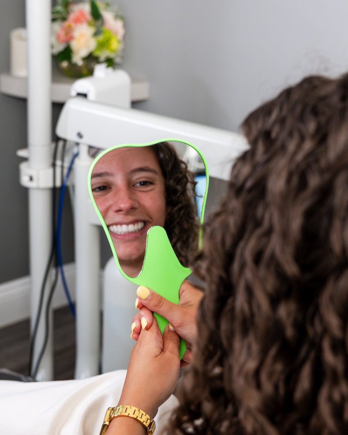 Patient smiling into a hand mirror after her visit